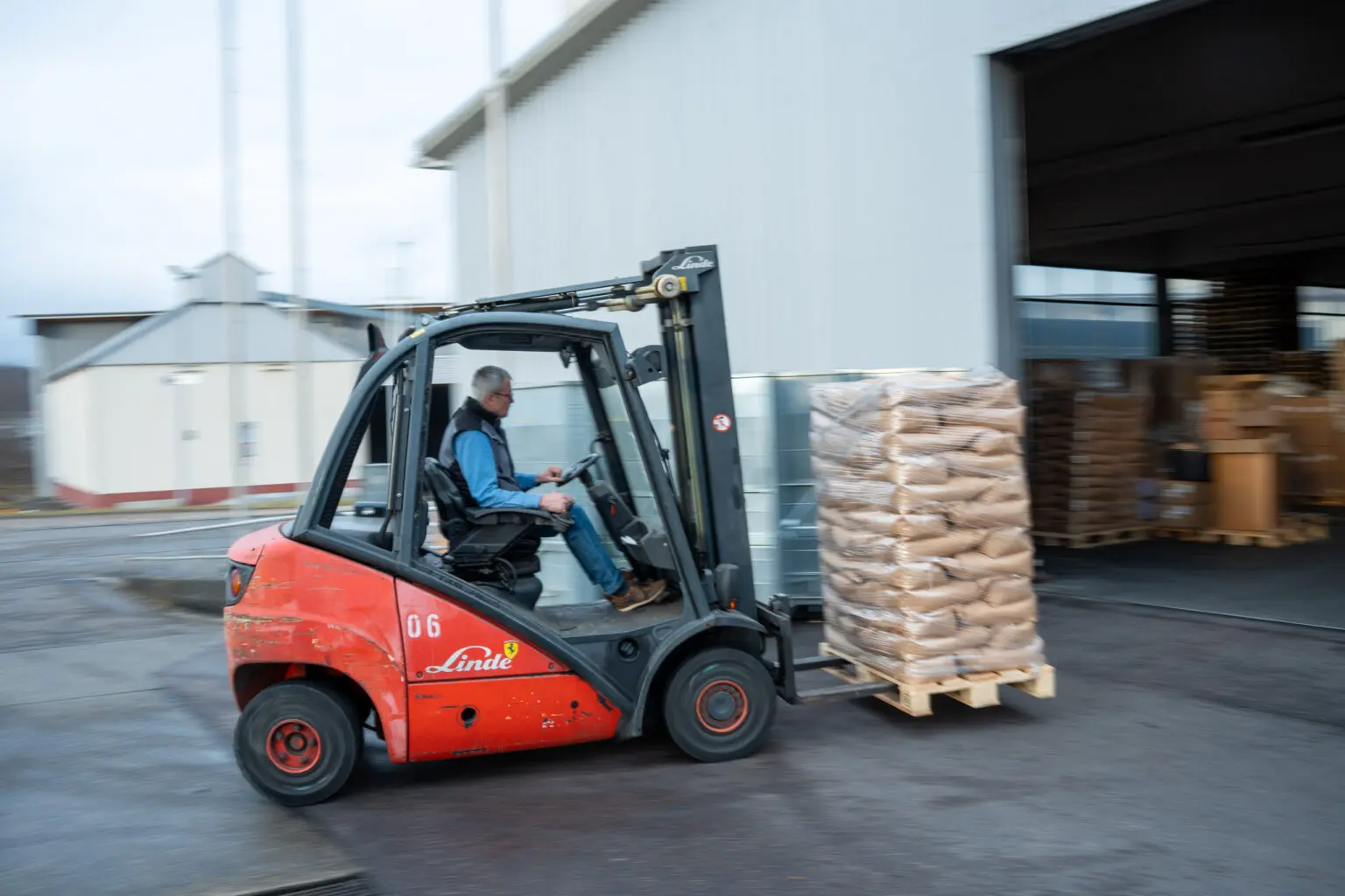 Mitarbeitender fährt einen Gabelstapler mit beladener Palette im Außenbereich.