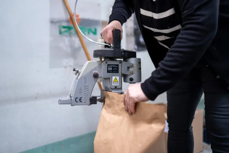 Mitarbeiterin verschließt einen Papiersack mit einer Sacknähmaschine.