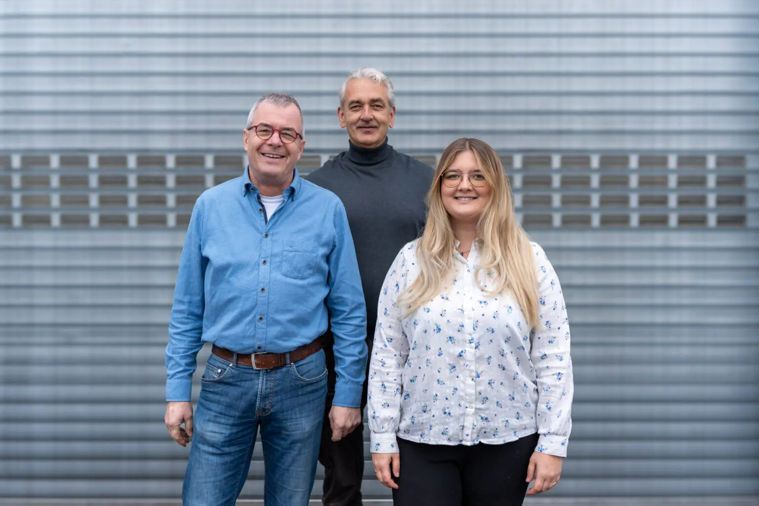 Drei Mitarbeitende vor einem Hallentor, frontal aufgenommen.