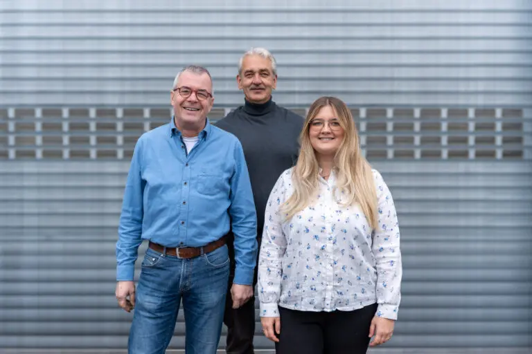 Drei Mitarbeitende vor einem Hallentor, frontal aufgenommen.