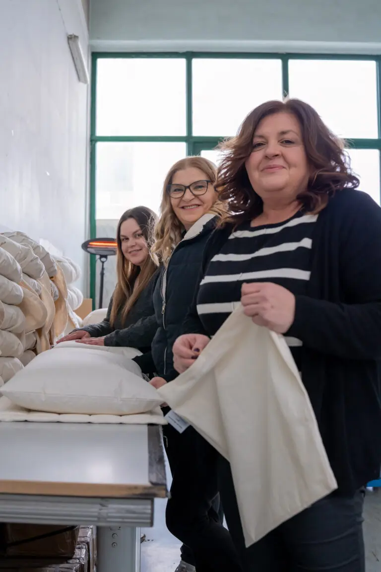 Drei Mitarbeitende an einem Arbeitstisch bei der Vorbereitung von Kissenbezügen.