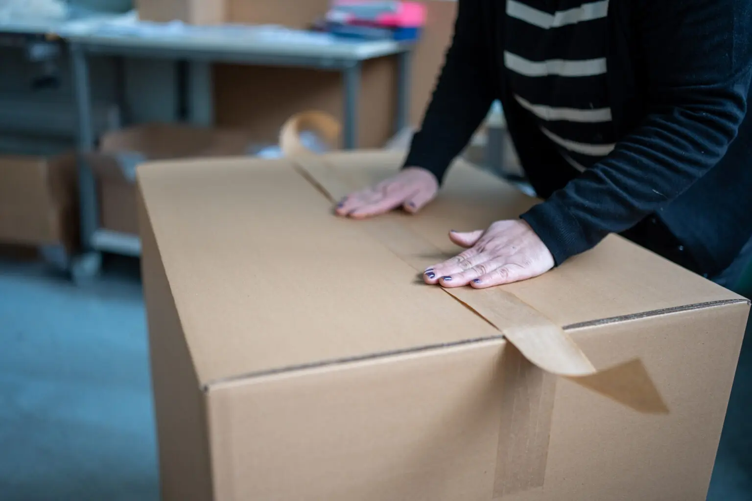 Hände beim Verschließen eines Versandkartons mit Klebeband.